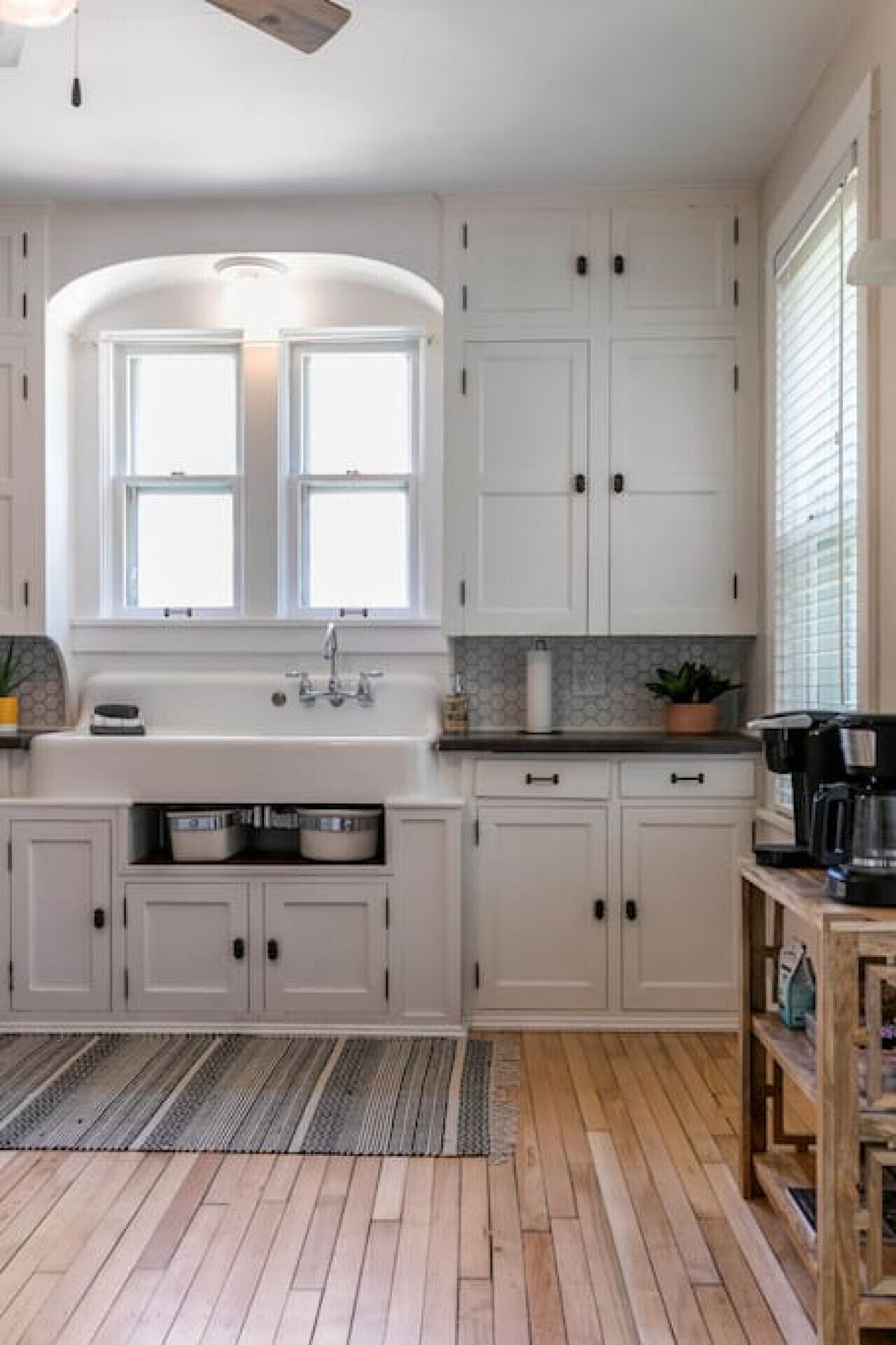 A kitchen with white cabinets, a window, a sink, and a coffee maker.
