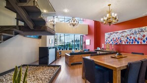 Ein modernes Interieur mit einem Holztisch, dunklen Polsterstühlen, einer Treppe und einem großen, abstrakten Gemälde an der Wand.