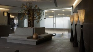 Eine moderne Lobby mit Sitzgelegenheit, einer großen Pflanze und hohen Stehlampen.