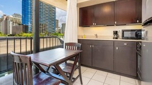 A compact kitchen with dark cabinets, a microwave, and a coffee maker. There is a dining table with chairs, and a large window offering a city view.