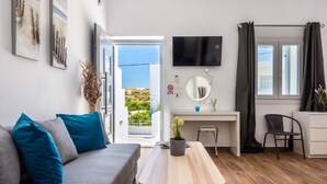 Ein modernes Wohnzimmer mit einem grauen Sofa, einem Holztisch, einem Schreibtisch und einem an der Wand befestigten Fernseher.