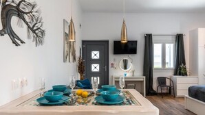 Ein Essbereich mit einem Holztisch, gedeckt für vier Personen, blauen Schüsseln und Gläsern. Ein Fernseher ist an der Wand montiert, und es gibt eine Tür mit einem Fenster.