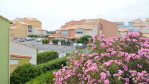 A residential area with houses, a parking lot, and a pink flowering bush. - Seaside Apartment: 2 Rooms, Sleeps 5, Modern, 50m from Beach, A/C, Parking Included (Narbonne)