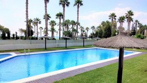 Une piscine entourée d’une pelouse, de palmiers et d’une structure à toit de chaume.