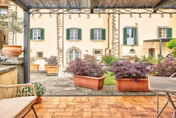 Une cour agrémentée de jardinières en terre cuite, d’une pergola et d’un espace aménagé pour s’asseoir.