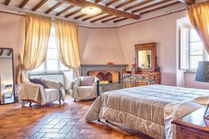 A bedroom with a bed, a chair, a fireplace, and a mirror.