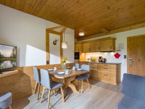 Une table à manger en bois avec des chaises, un coin cuisine avec des meubles en bois et un tableau accroché au mur.