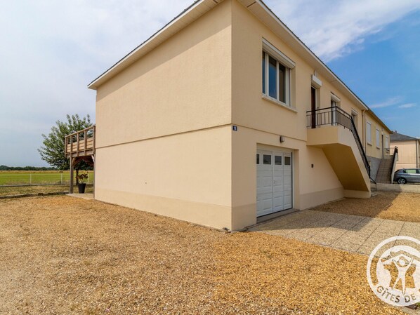 Un immeuble de deux étages avec une porte de garage blanche, un balcon et un escalier menant à l’étage supérieur.
