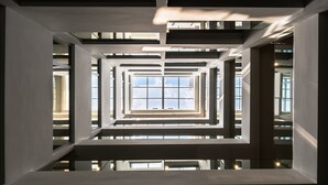 Ein modernes architektonisches Interieur mit einem zentralen, offenen Raum, der von geometrischen Formen und großen Fenstern gestaltet wird.