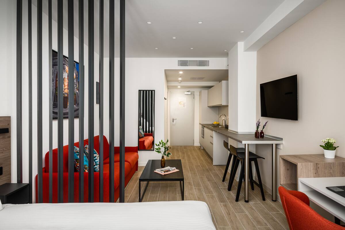 Een moderne hotelkamer met een bed, een rode bank, een kleine tafel en een kitchenette.
