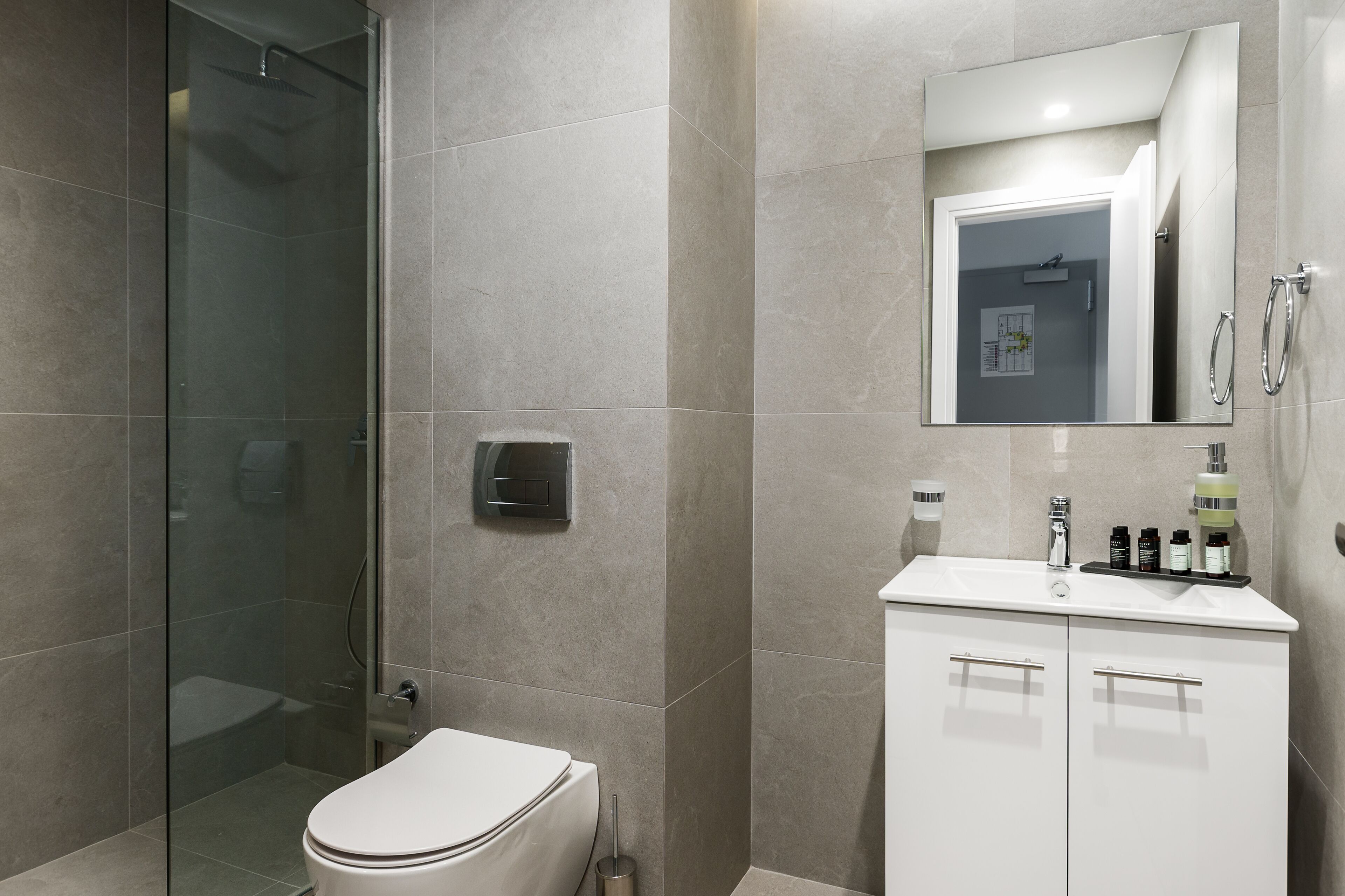 A modern bathroom with a glass-enclosed shower, a white toilet, and a vanity with a mirror and toiletries.