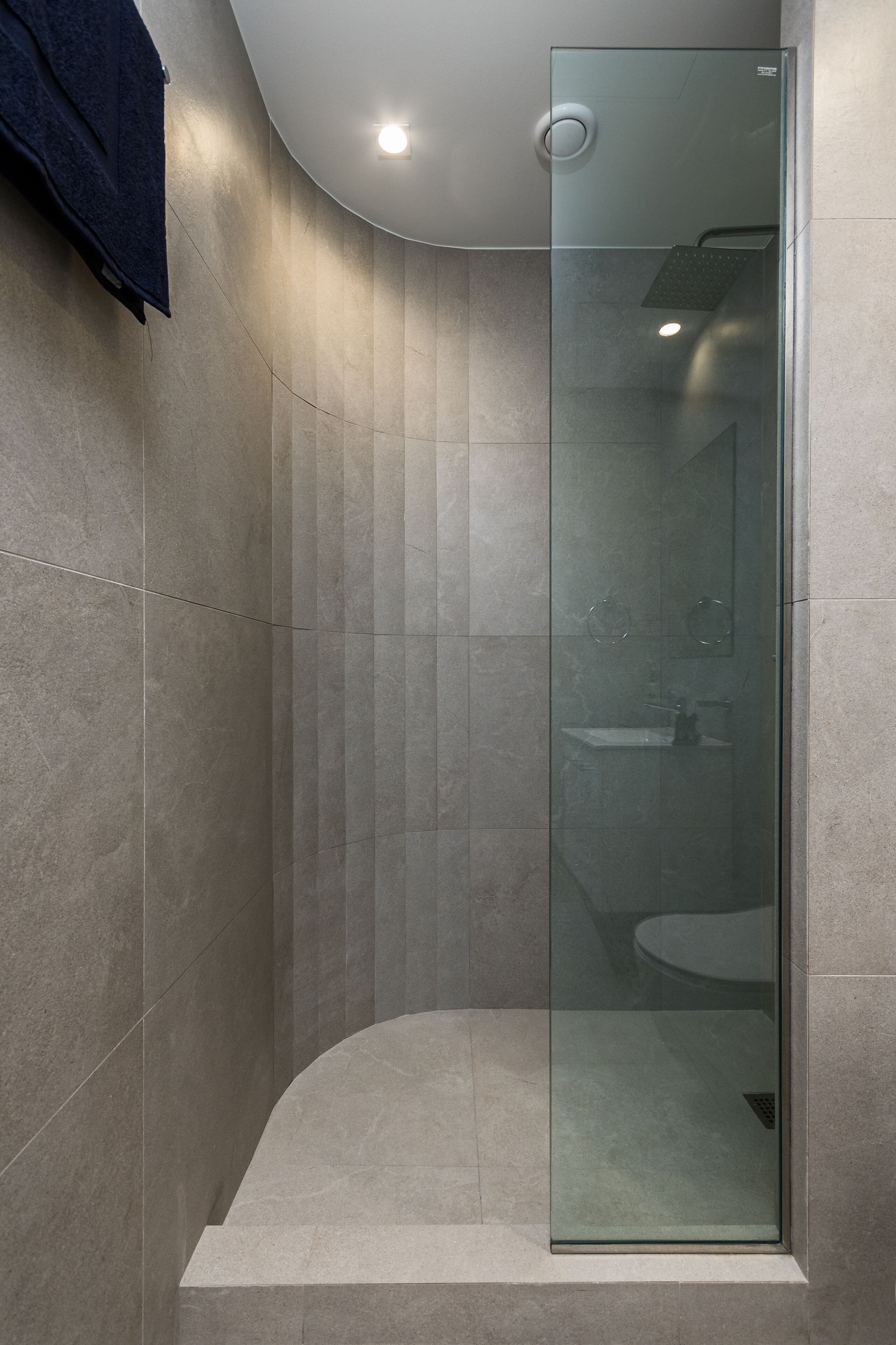 Un bagno moderno con cabina doccia in vetro, soffitto curvo e zona lavabo a vista.