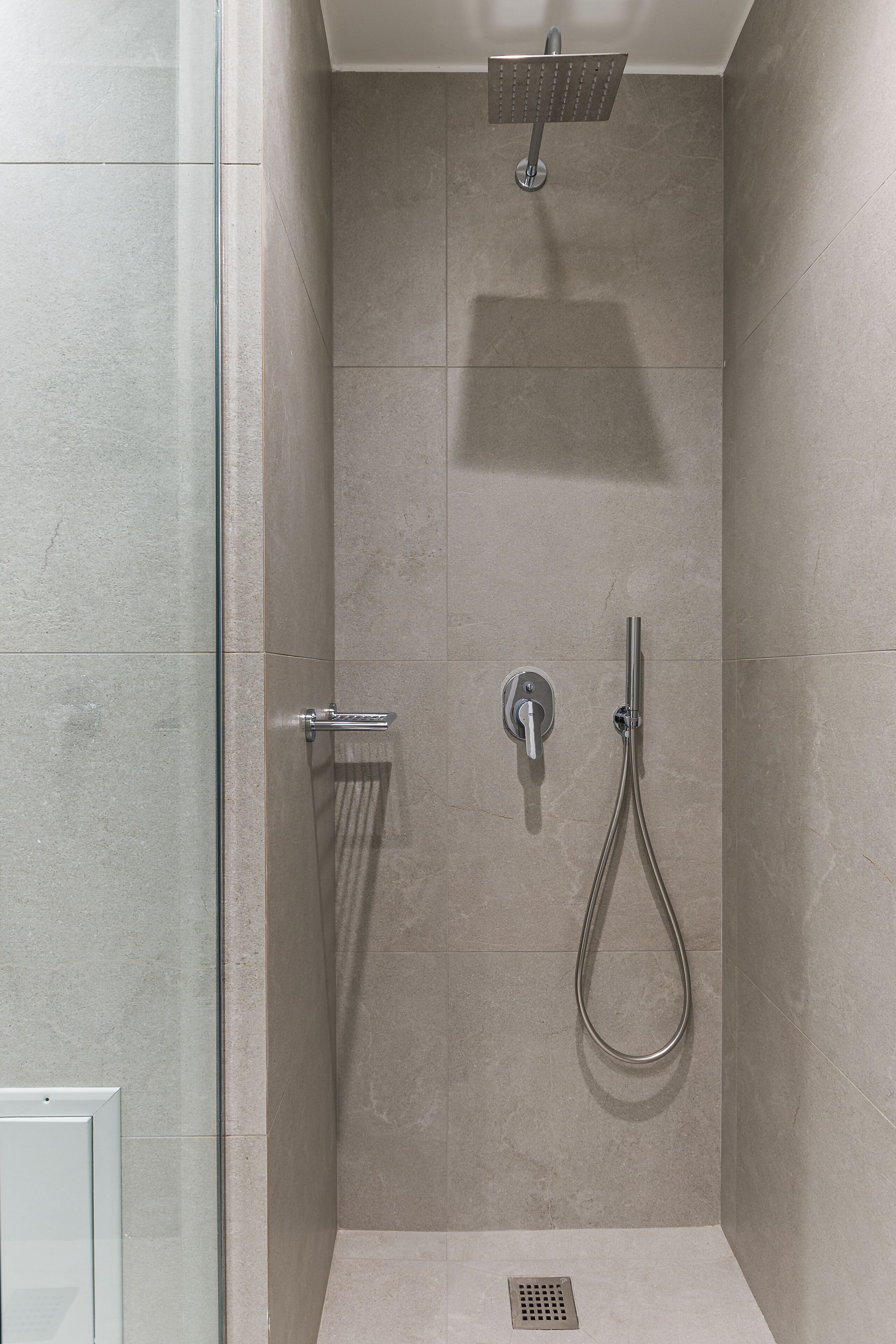 A modern shower with a glass door, a handheld showerhead, and a wall-mounted faucet.