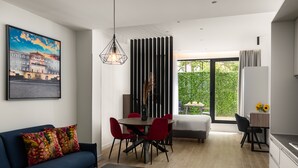 Ein modernes Wohnzimmer mit einem blauen Sofa, roten Sesseln, einem Esstisch und einem großen Fenster mit Blick ins Grüne.