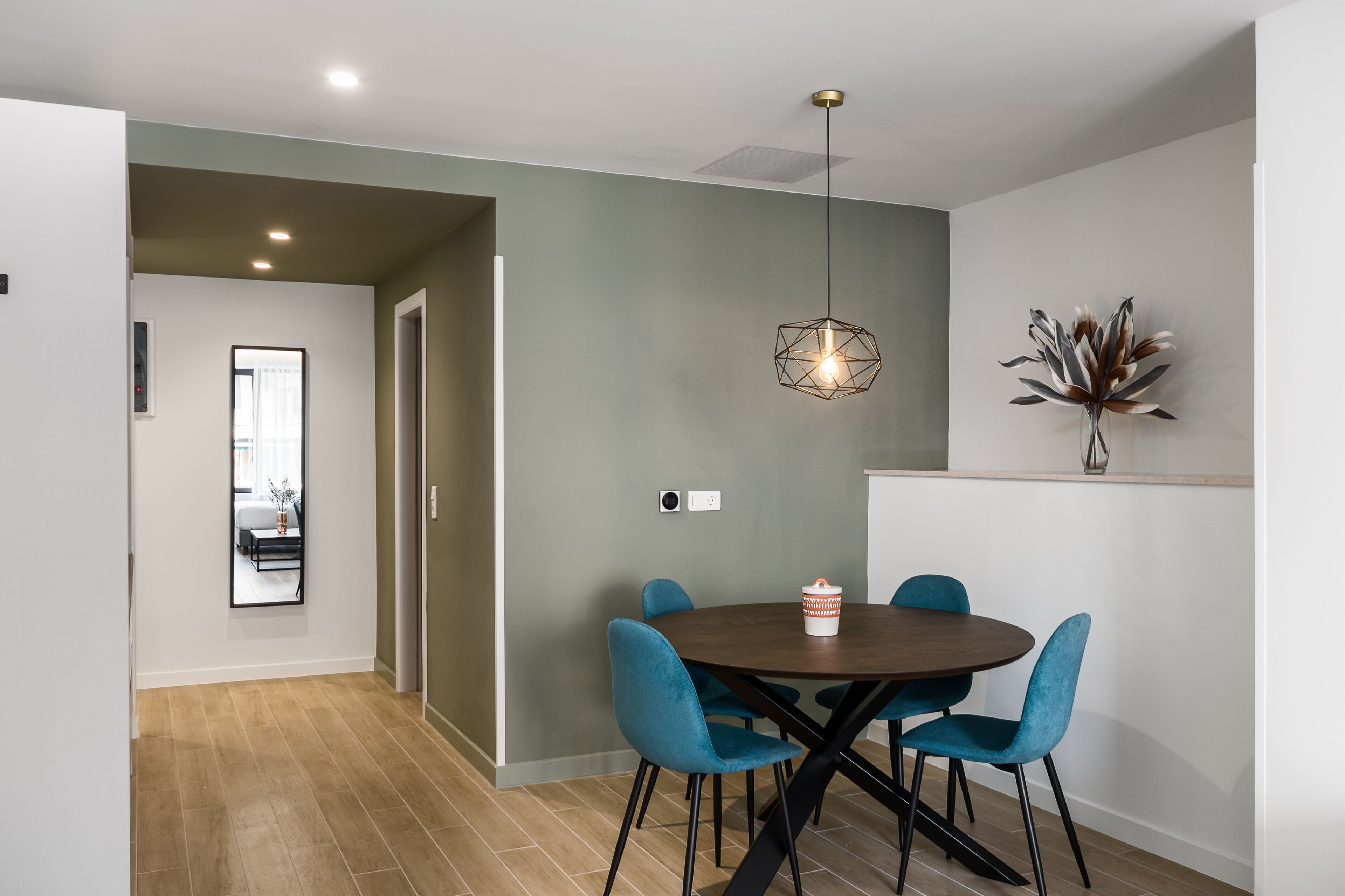 A dining area with a round table, four blue chairs, and a pendant light.