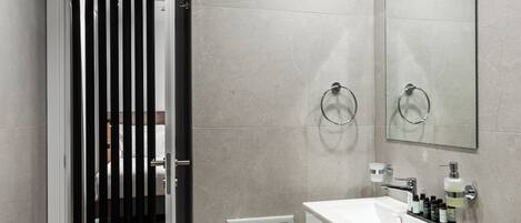 A modern bathroom with a white sink, mirror, and towel rings.