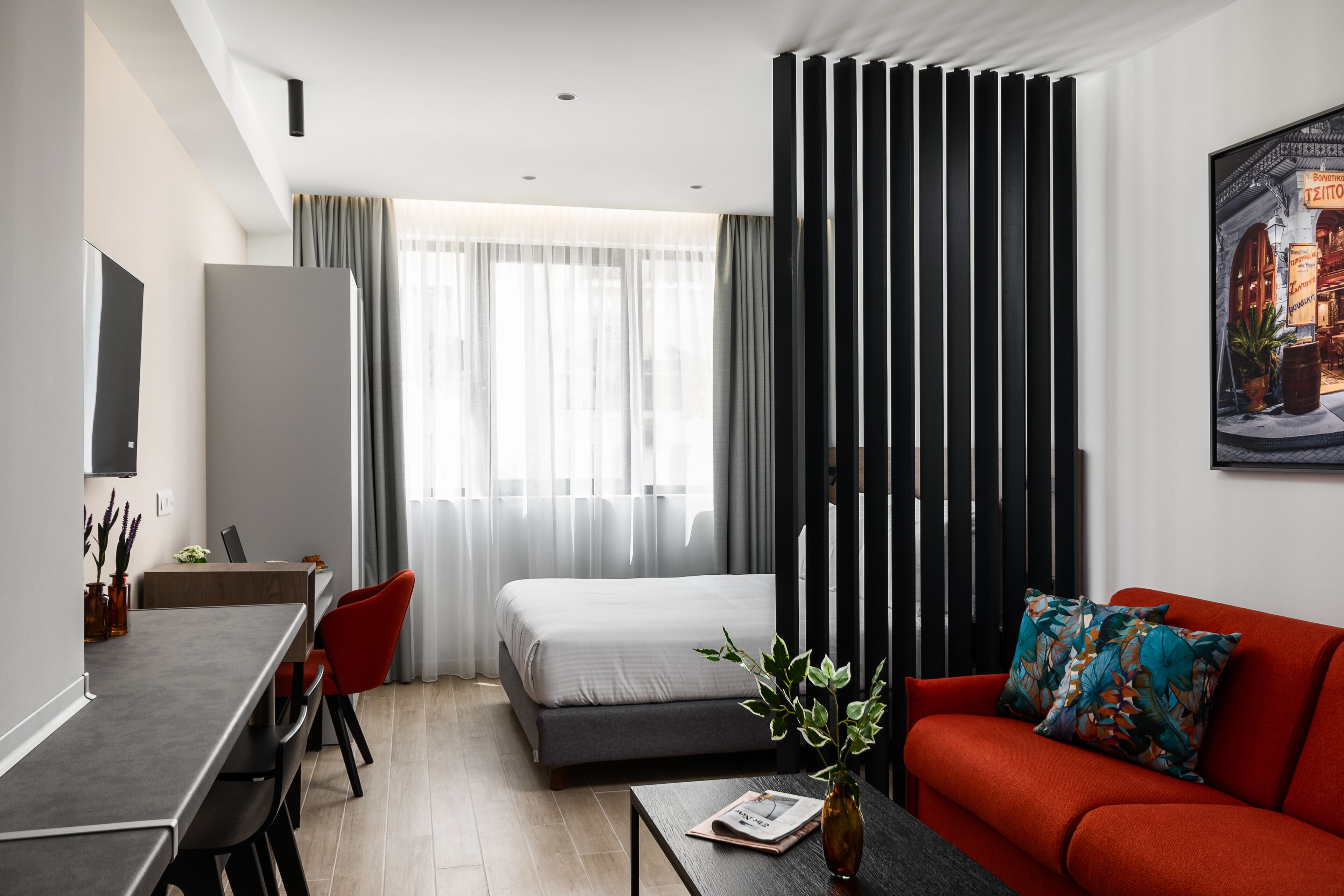 A modern hotel room with a bed, a sofa, a desk, and a dining area.