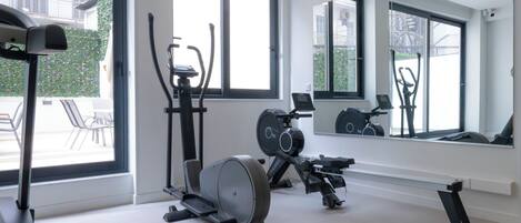 A modern gym with various exercise equipment, large windows, and a mirror reflecting the equipment.