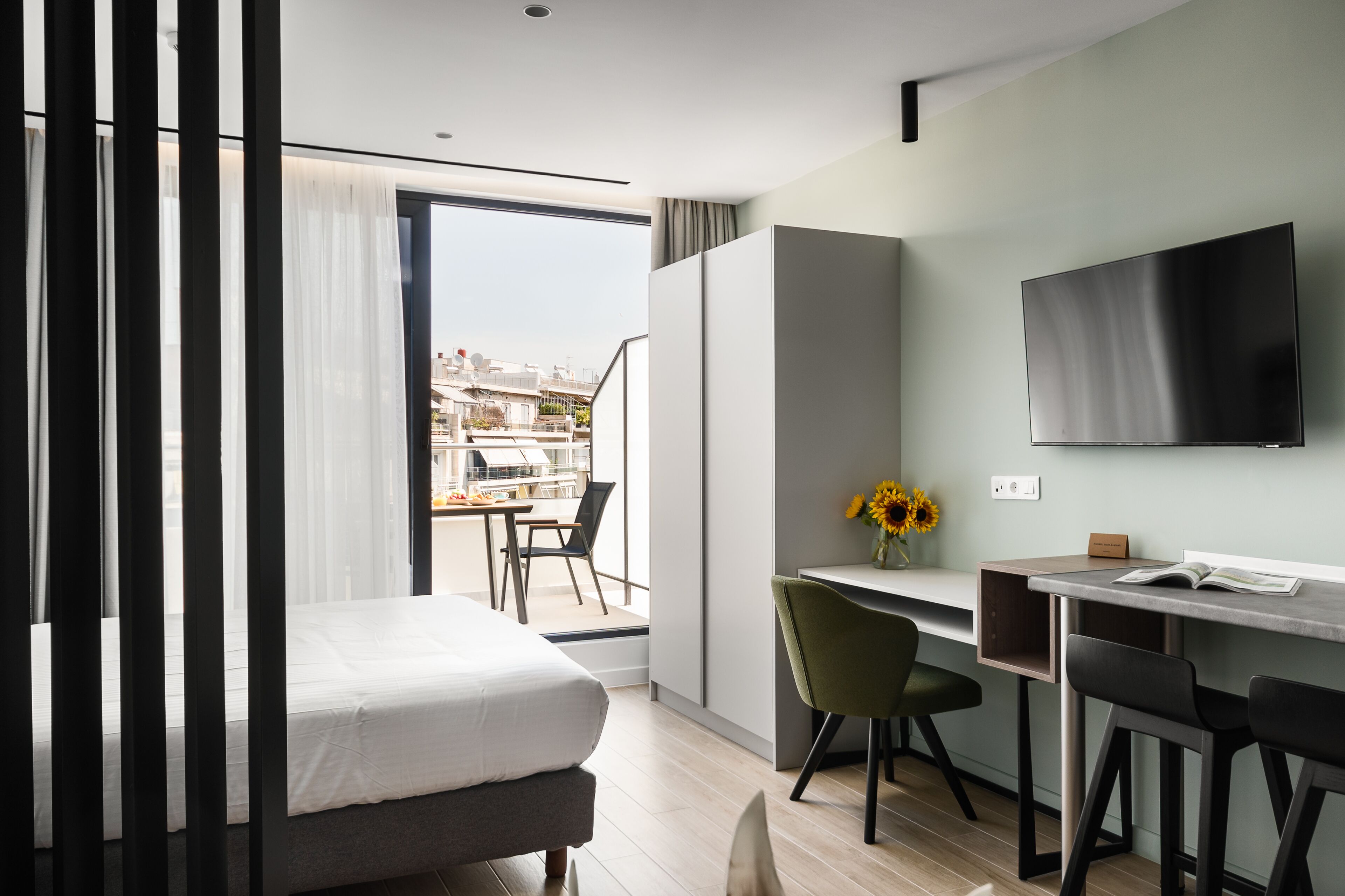 Una habitación de hotel moderna con cama, escritorio, televisión y balcón con vista a la ciudad.