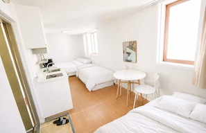 A compact hotel room with a kitchenette, a bed, a small table, and a chair.