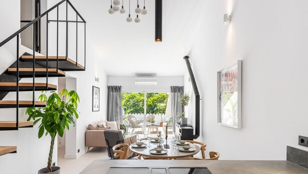Une cuisine moderne dotée d’un îlot central, d’un escalier avec des rampes noires et d’un coin repas comprenant une table ronde et des chaises.