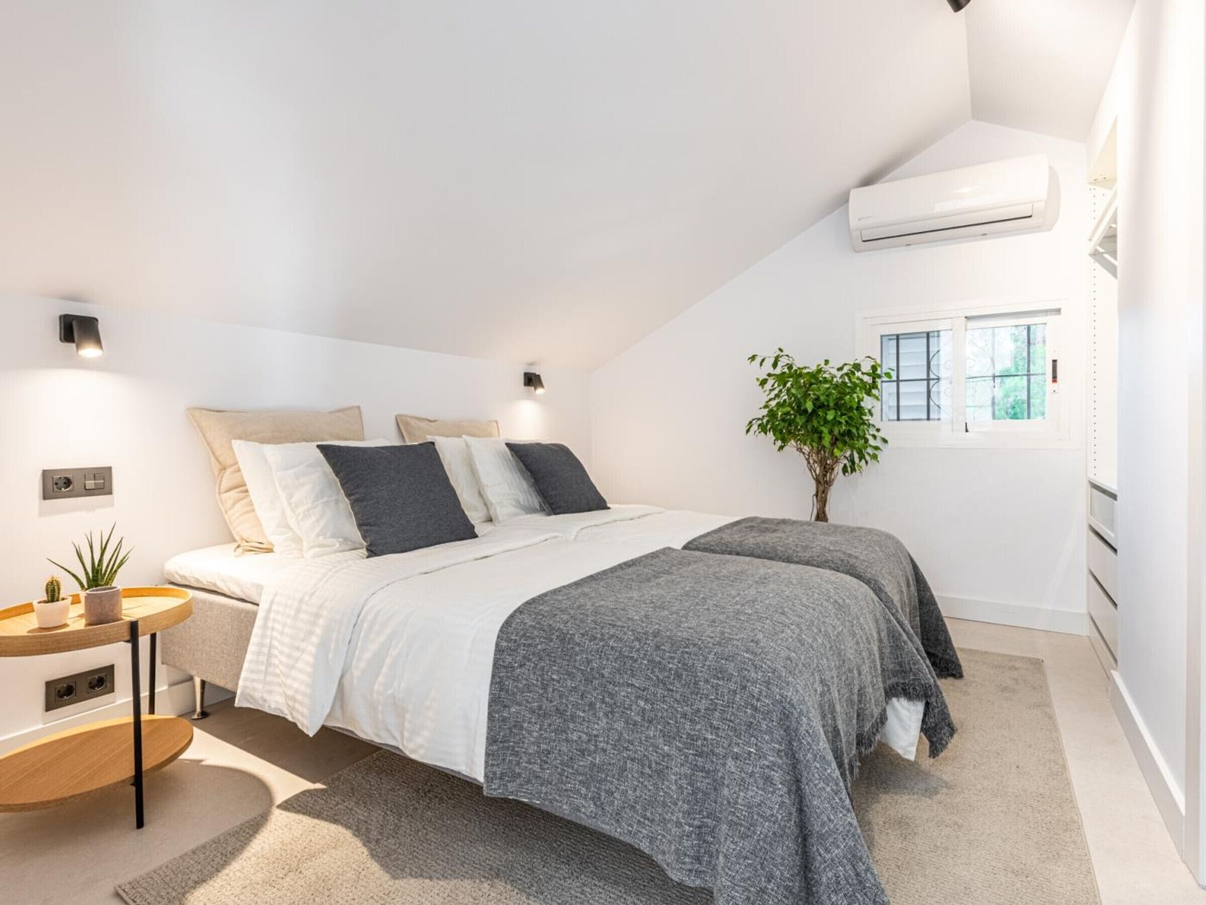 Ein modernes Schlafzimmer mit Bett, Nachttischen, einer kleinen Pflanze und einer Klimaanlage.