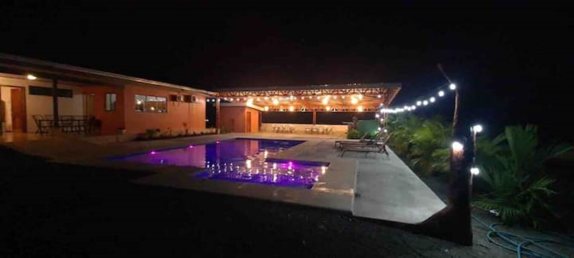 A pool area with a water feature, surrounded by a building with string lights.