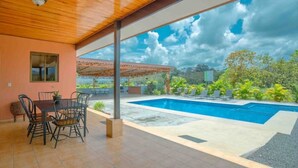 Un patio techado con piscina, mobiliario exterior y vistas del paisaje circundante.