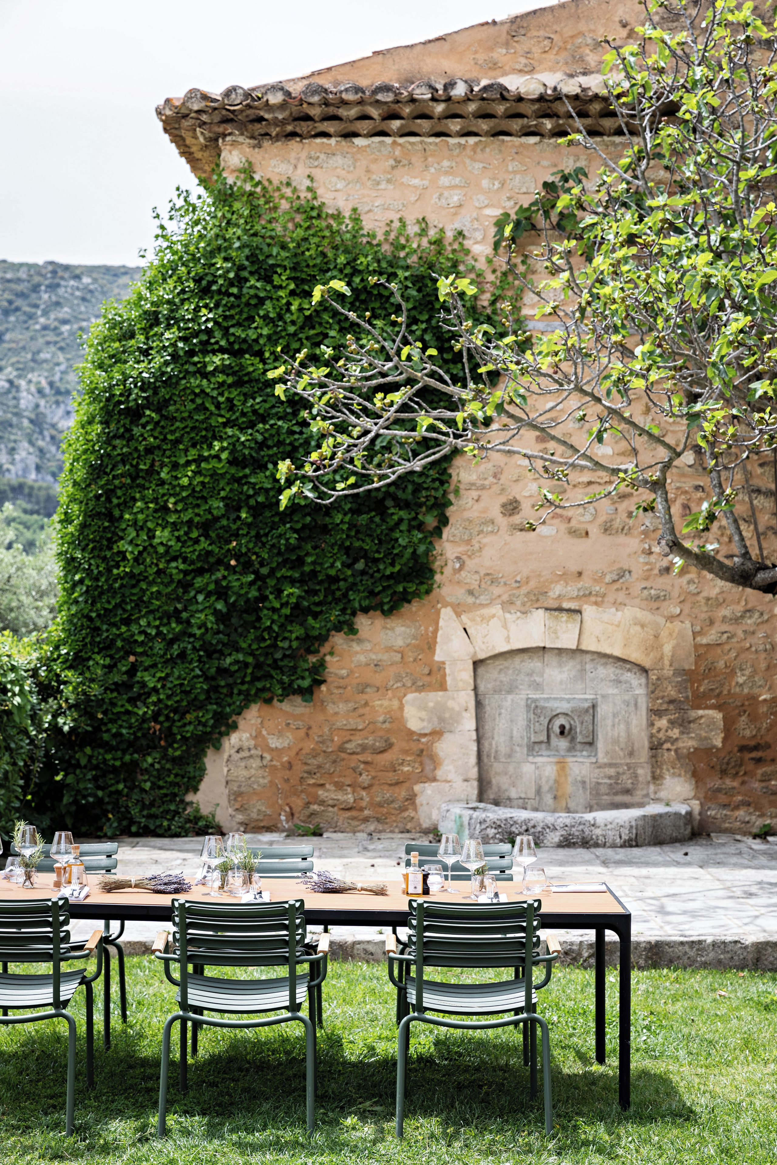 Un espace extérieur aménagé pour les repas, avec un mur en pierre, une table en bois entourée de chaises et une vue sur un paysage montagneux.