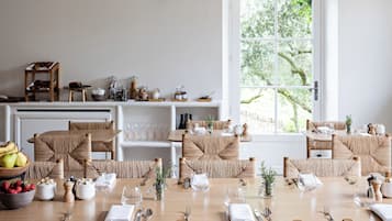Un espace repas avec une longue table en bois, des chaises en osier et des lampes suspendues.