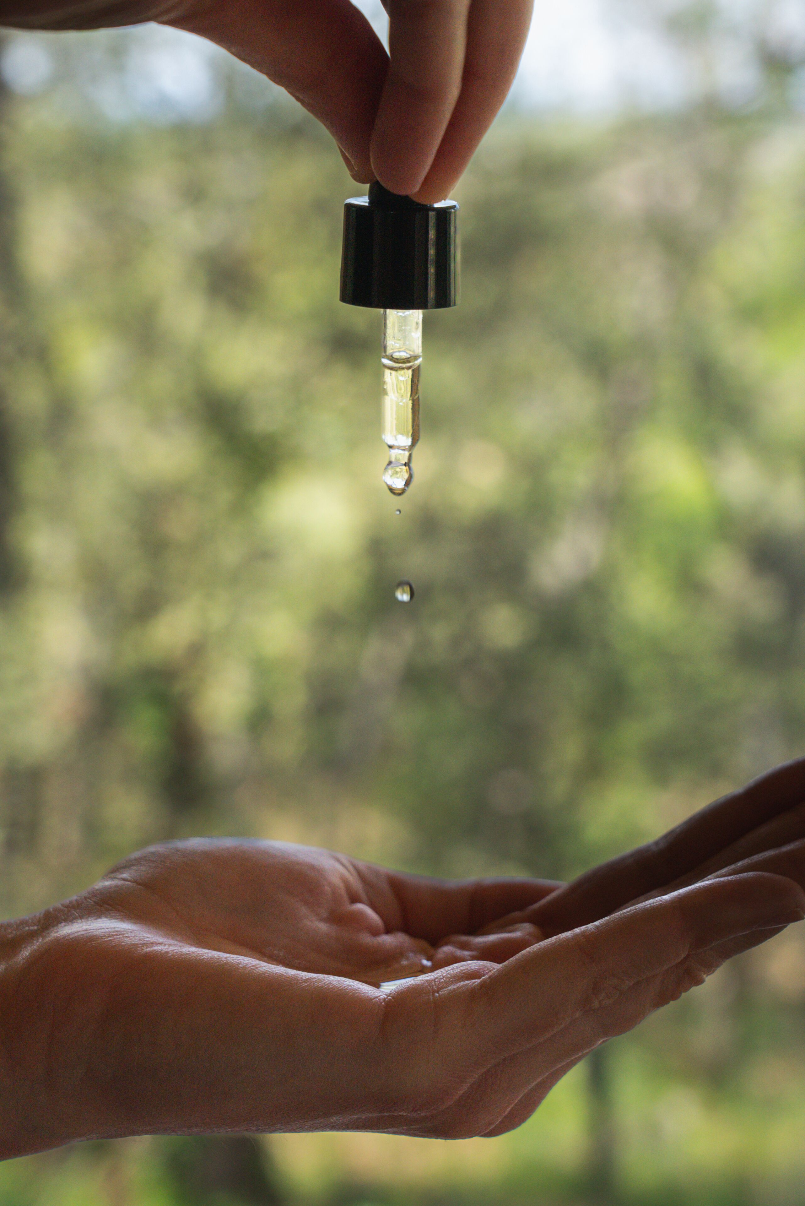 Een hand vasthoudt een druppelaar met vloeistof, en een andere hand erboven.