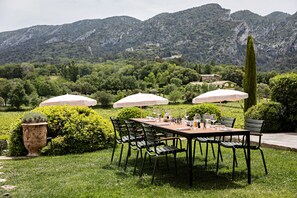 An outdoor dining area with a table set for six, surrounded by chairs, with umbrellas providing shade. - Bastide du Mourre - Fontenille Collection (Oppede)