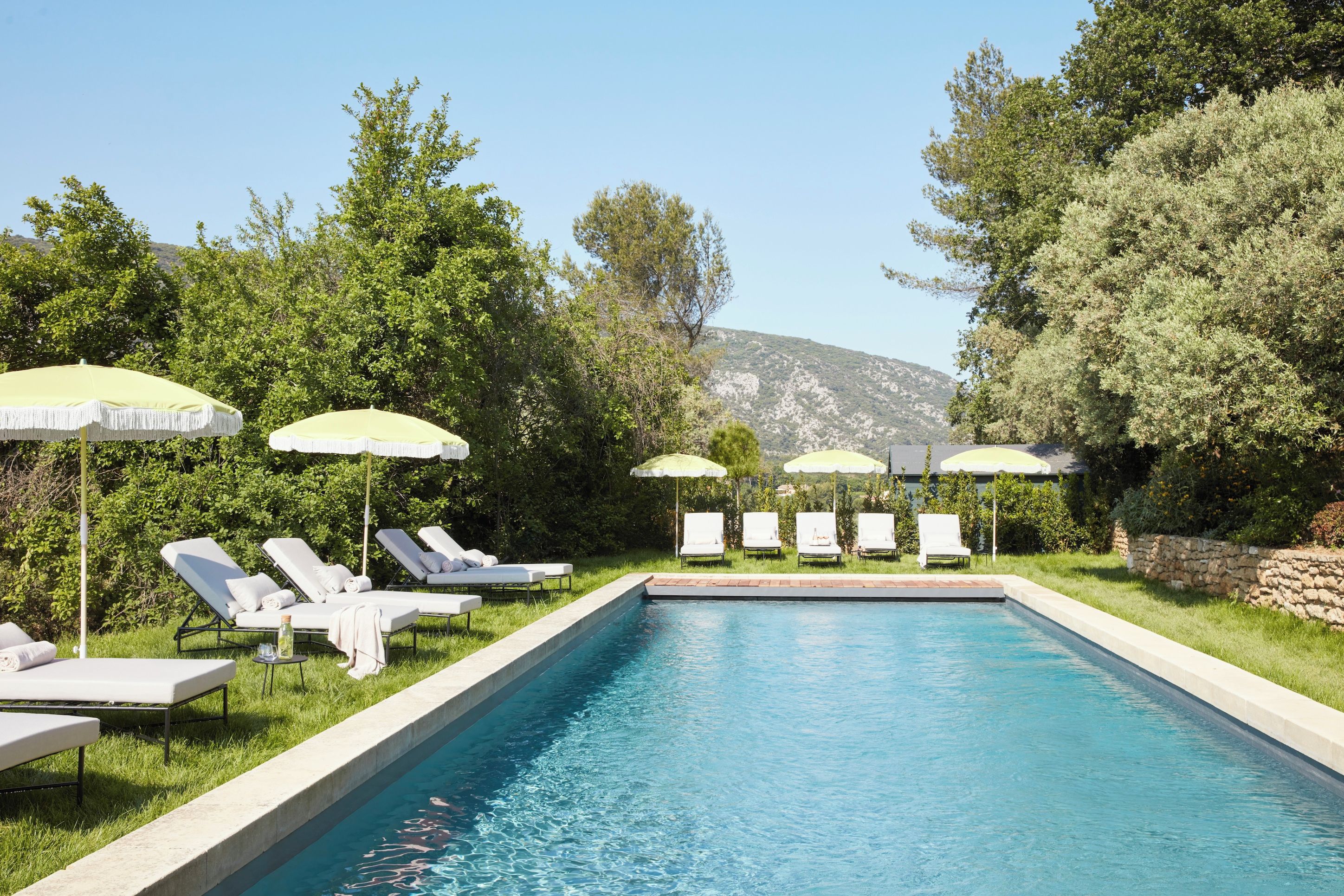 A swimming pool with lounge chairs and umbrellas, surrounded by greenery and hills.