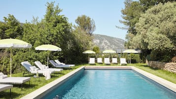 A swimming pool with lounge chairs and umbrellas, surrounded by greenery and hills.