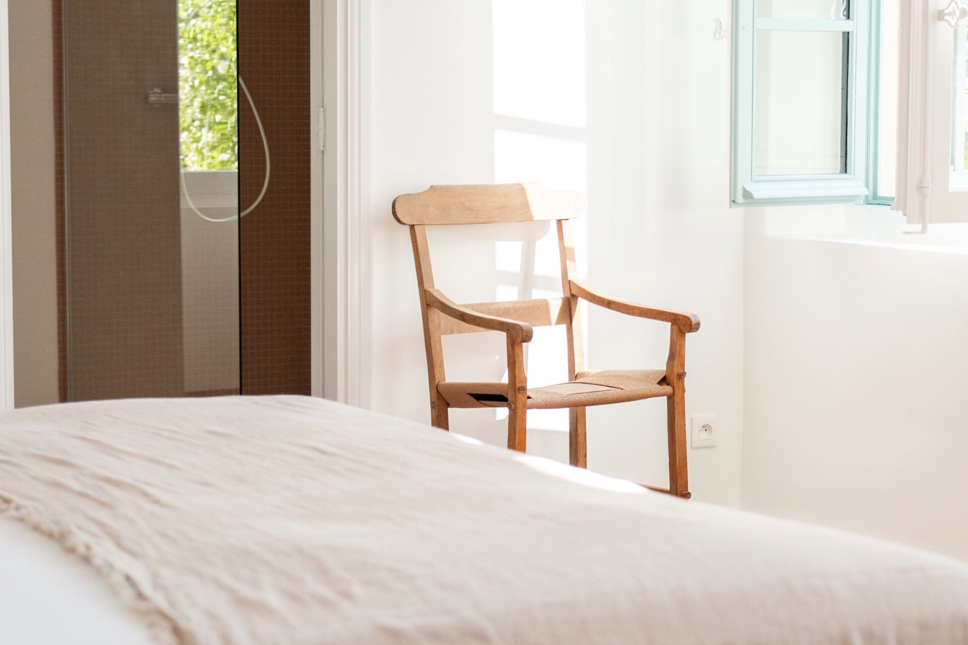 A bedroom with a bed, a wooden chair, a window, and a door.