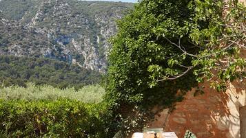 An outdoor dining area with a table and chairs, set against a backdrop of a mountainous landscape and a building with a tiled roof.