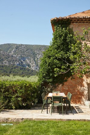 An outdoor dining area with a table and chairs, set against a backdrop of a mountainous landscape and a building with a tiled roof. - Bastide du Mourre - Fontenille Collection (Oppede)