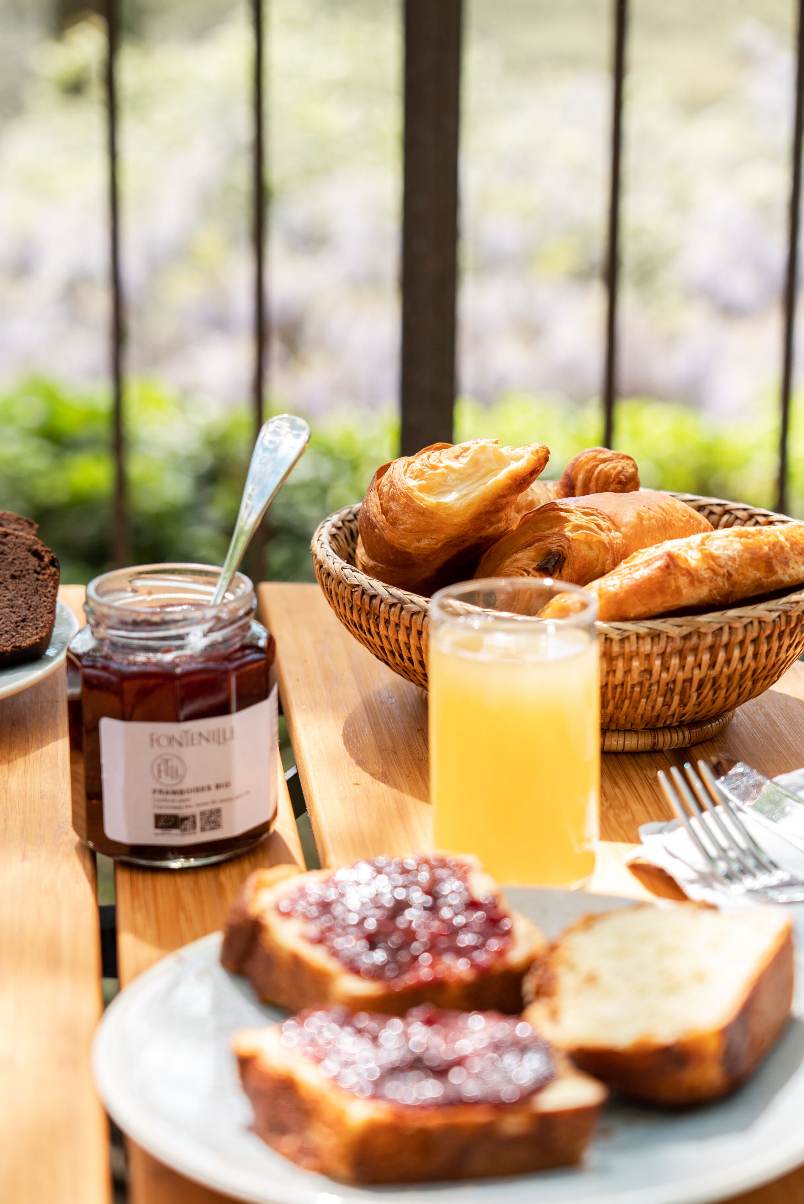 Une table en bois dressée pour le petit-déjeuner, avec du pain, des croissants, de la confiture et un verre de jus de fruits.