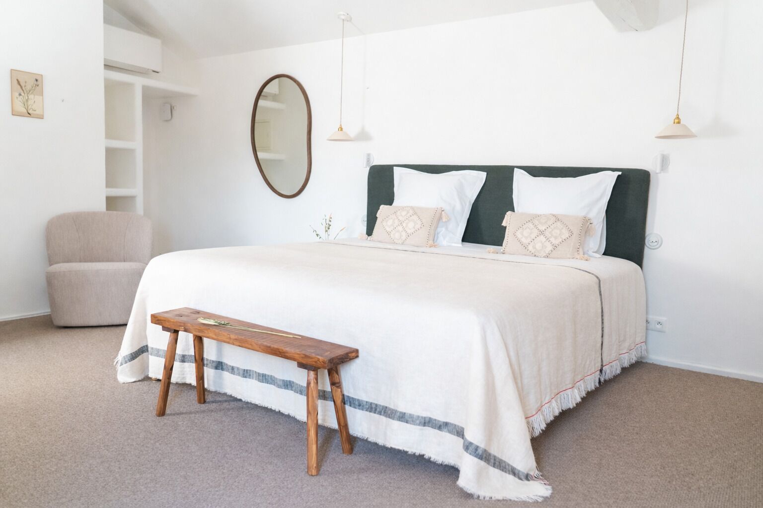 Een slaapkamer met een bed, een bankje, een stoel, een spiegel en hanglampen.