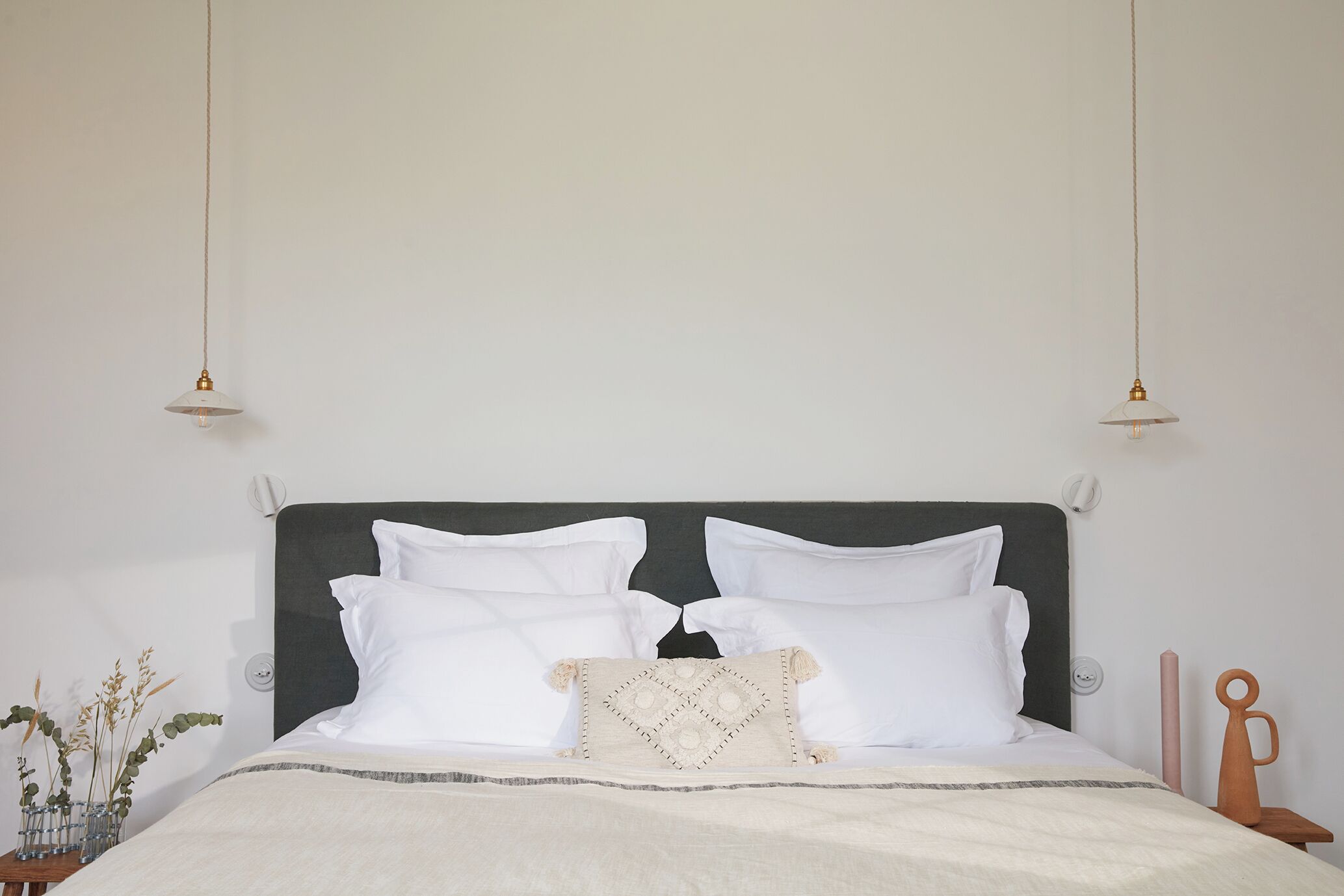 A bed with white bedding, a dark headboard, and two pendant lights.