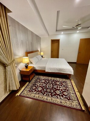 A hotel room with a bed, nightstands, a patterned rug, curtains, and a ceiling fan. - GOHO ROOMS Murree (Murree)
