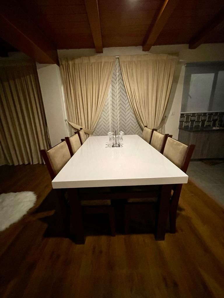 Un comedor con una mesa blanca, sillas de madera y cortinas.