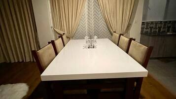 A dining area with a white table, wooden chairs, and curtains.