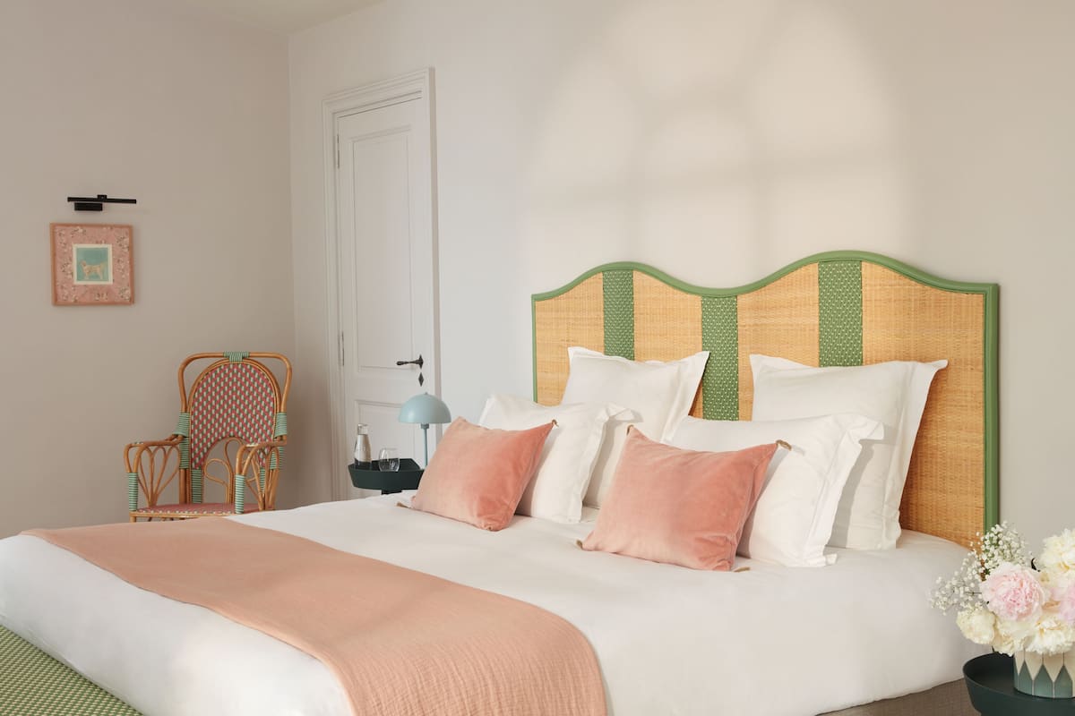 A neatly made bed with a green headboard, white bedding, and a peach-colored throw blanket.