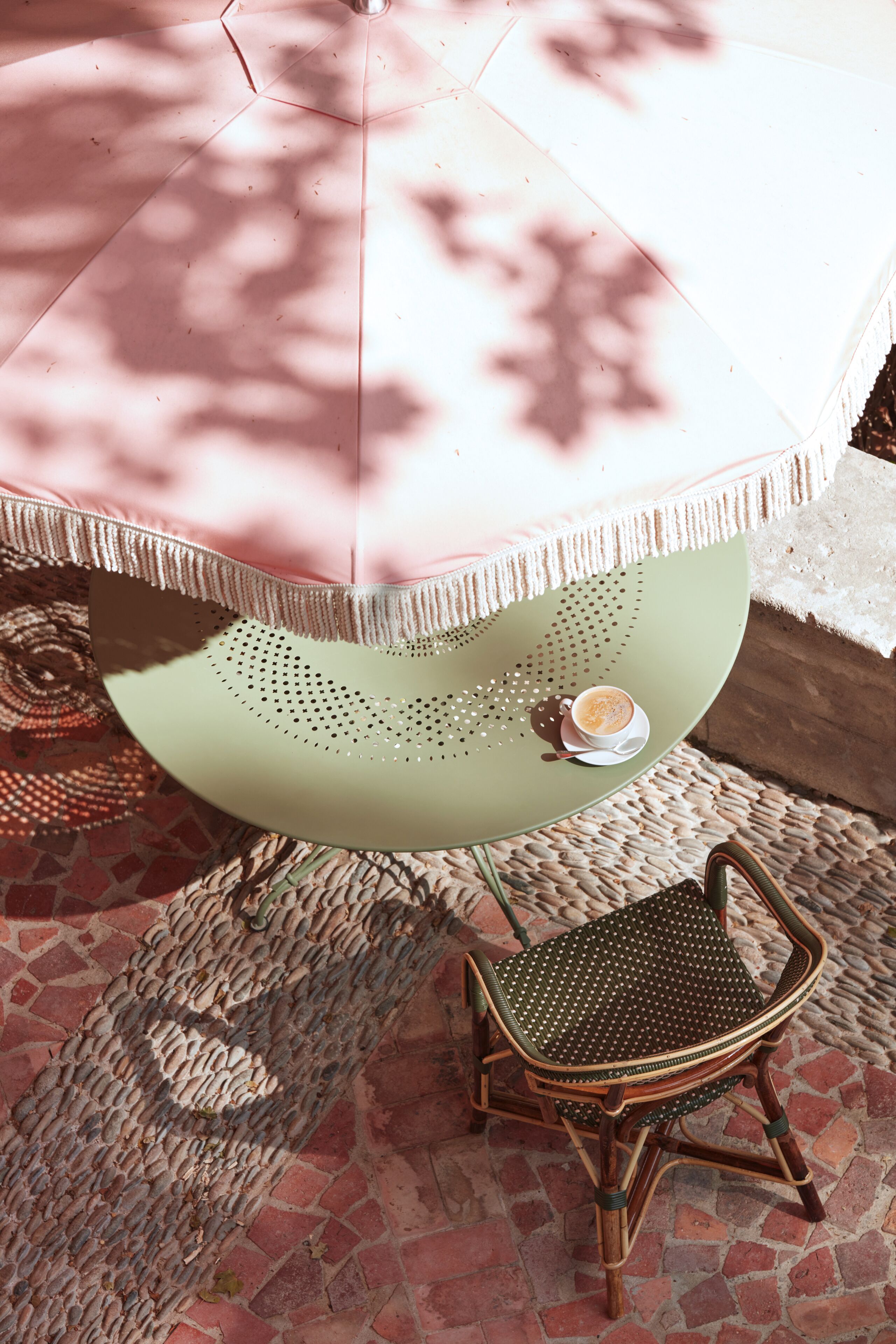 A round table with a green surface and a white umbrella overhead. A wicker chair is positioned in front of the table.