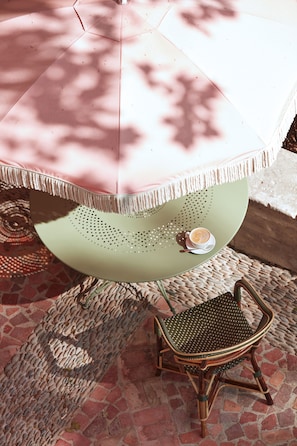 A round table with a green surface and a white umbrella overhead. A wicker chair is positioned in front of the table. - Domaine de Chalamon - Fontenille Collection (St.-Rémy-de-Provence)