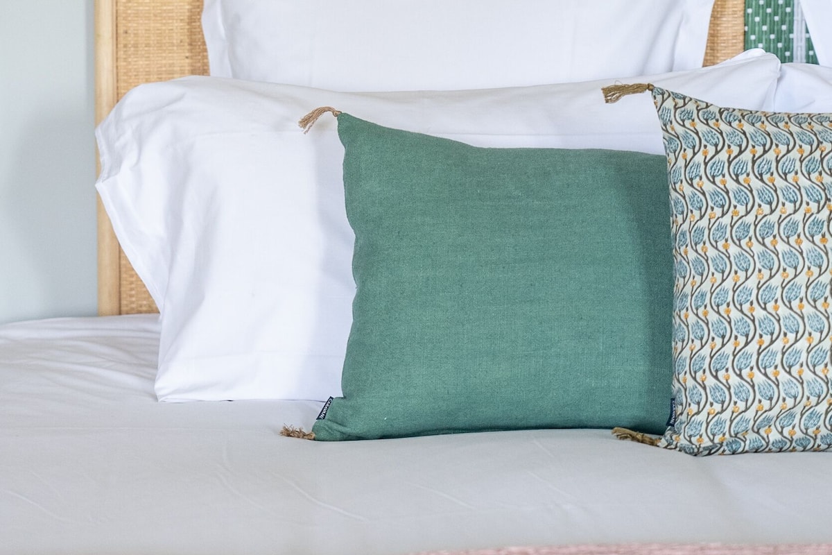 A bed with a woven headboard, white and green pillows, and a patterned pillow.