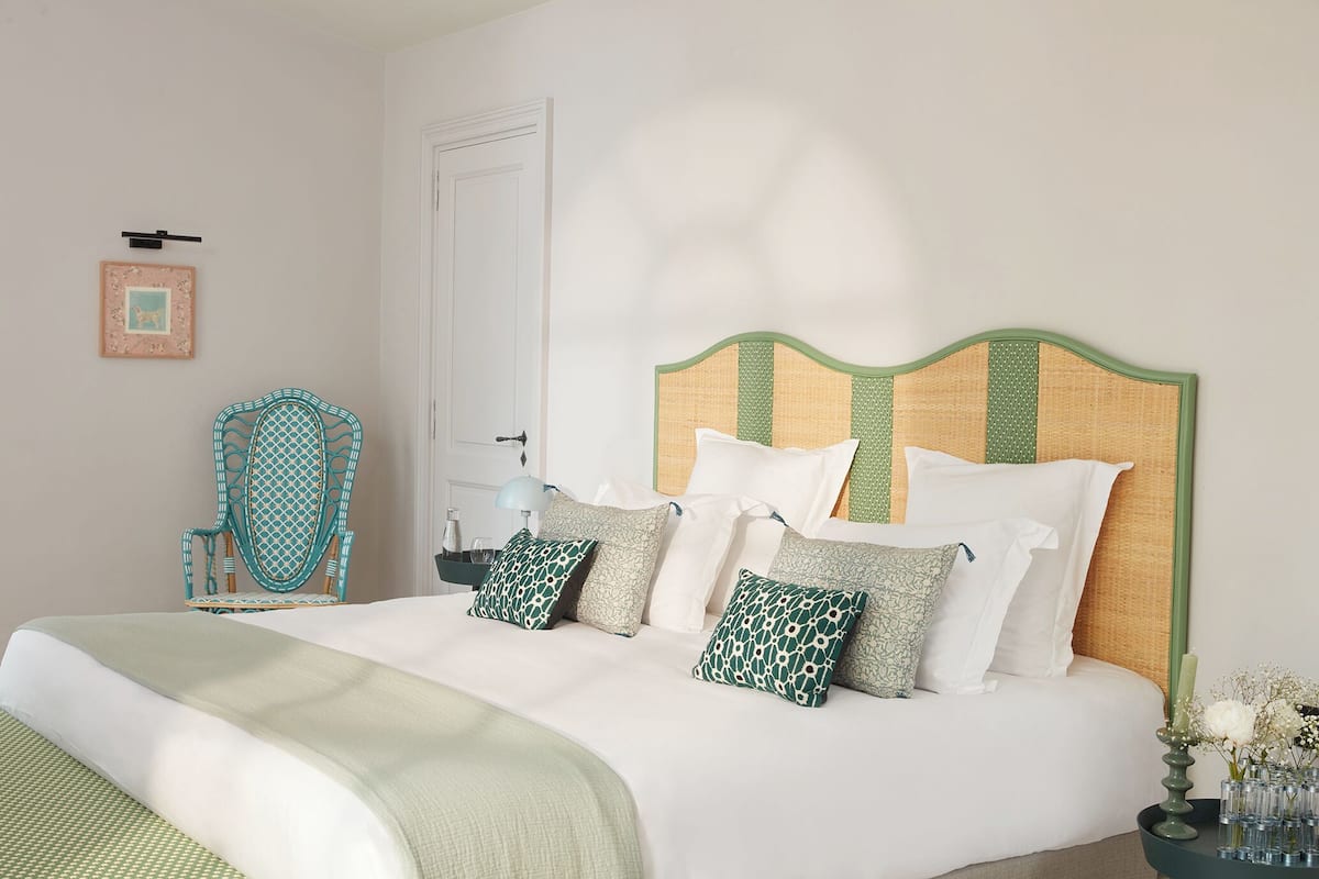 A neatly made bed with a patterned headboard, a chair with a geometric design, and a bedside table with a vase of flowers.