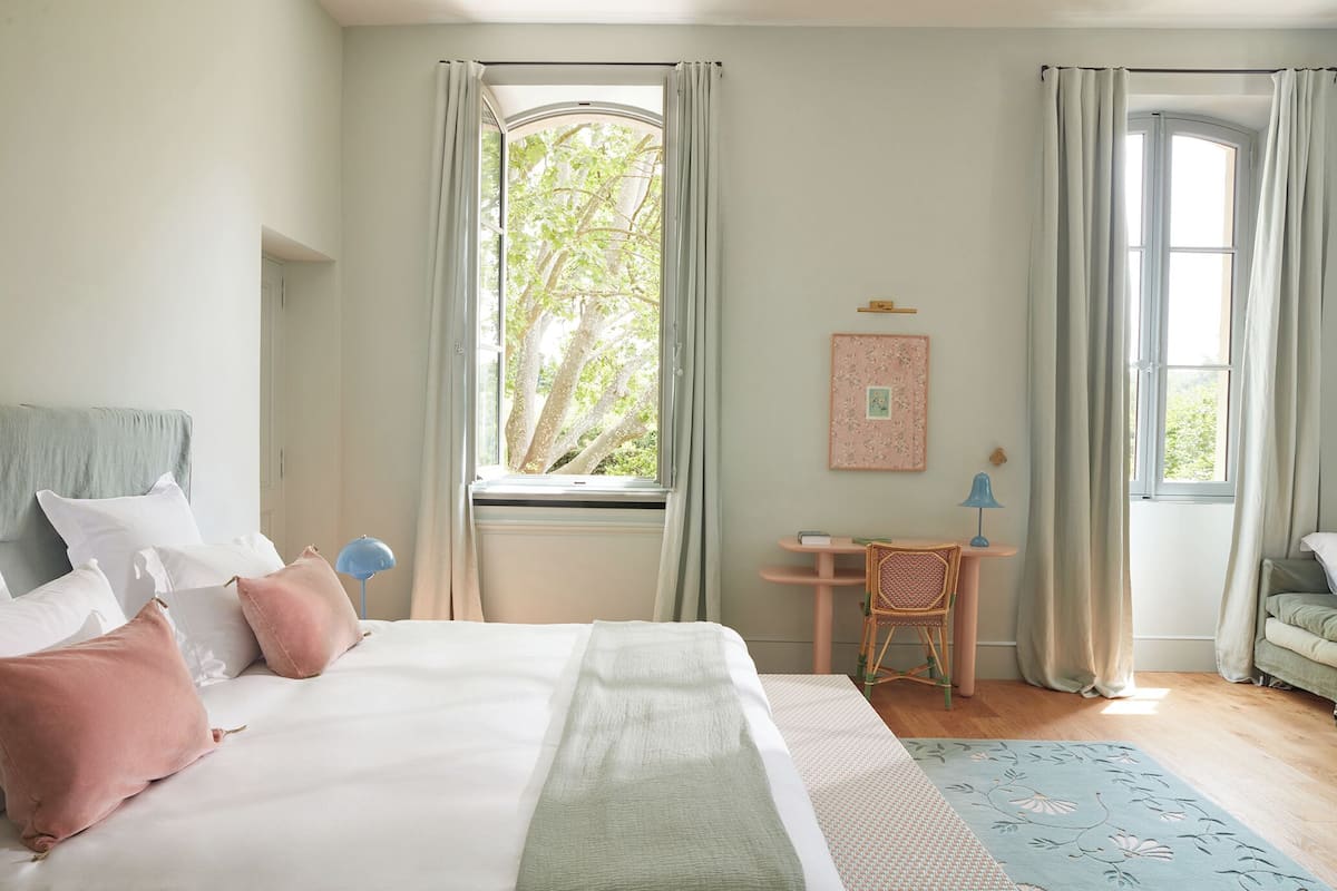 A bedroom with a bed, a chair, a desk, and a window with curtains.