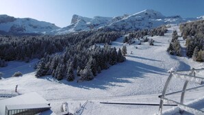 A snow-covered mountain landscape with a ski slope, trees, and a clear sky.